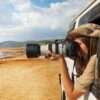 Side view portrait of young woman taking photo of Kenyan lake Nakuru from the open window of safari jeep