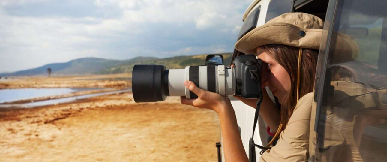 Side view portrait of young woman taking photo of Kenyan lake Nakuru from the open window of safari jeep