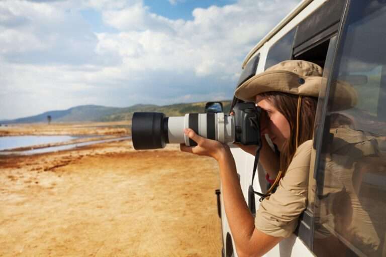 Side view portrait of young woman taking photo of Kenyan lake Nakuru from the open window of safari jeep